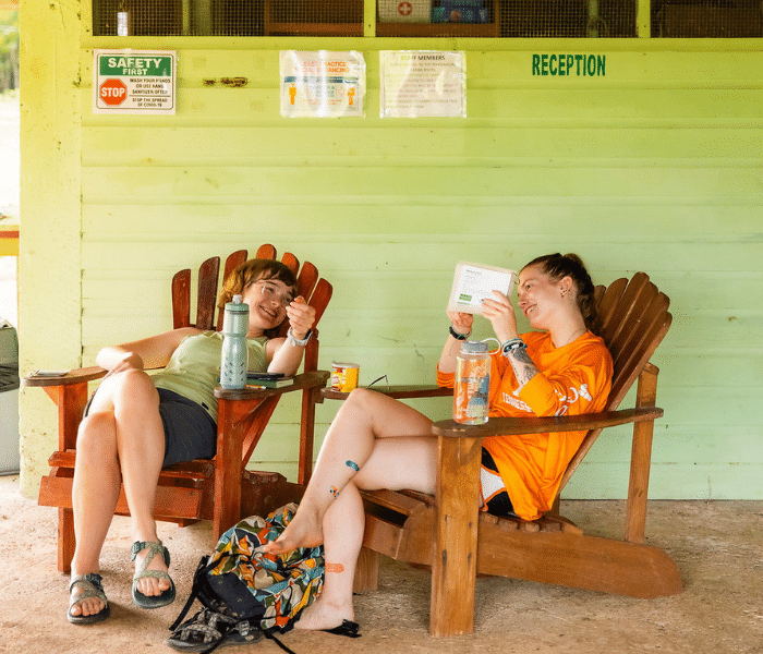 two female students in beach chairs over a green wall