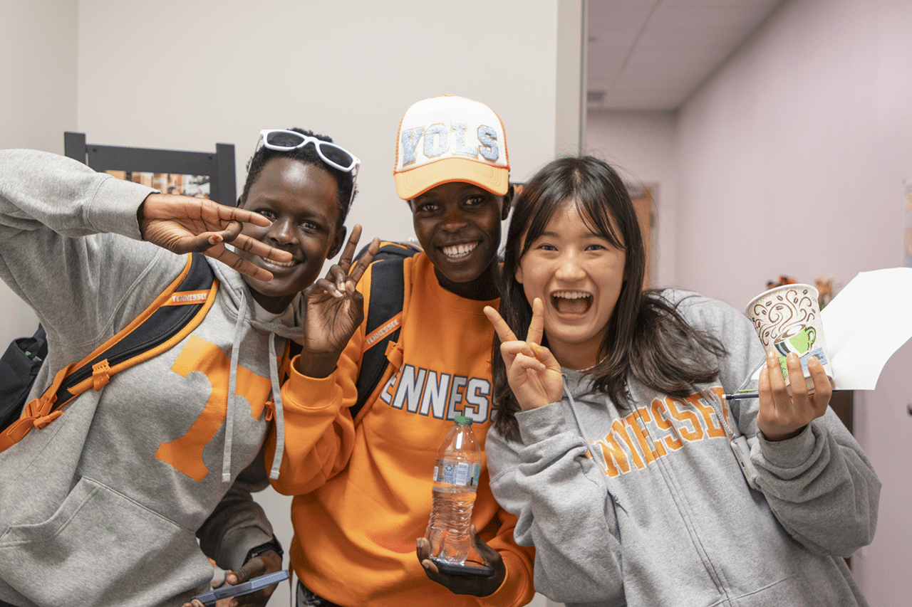 Three students smilie and make peace signs.