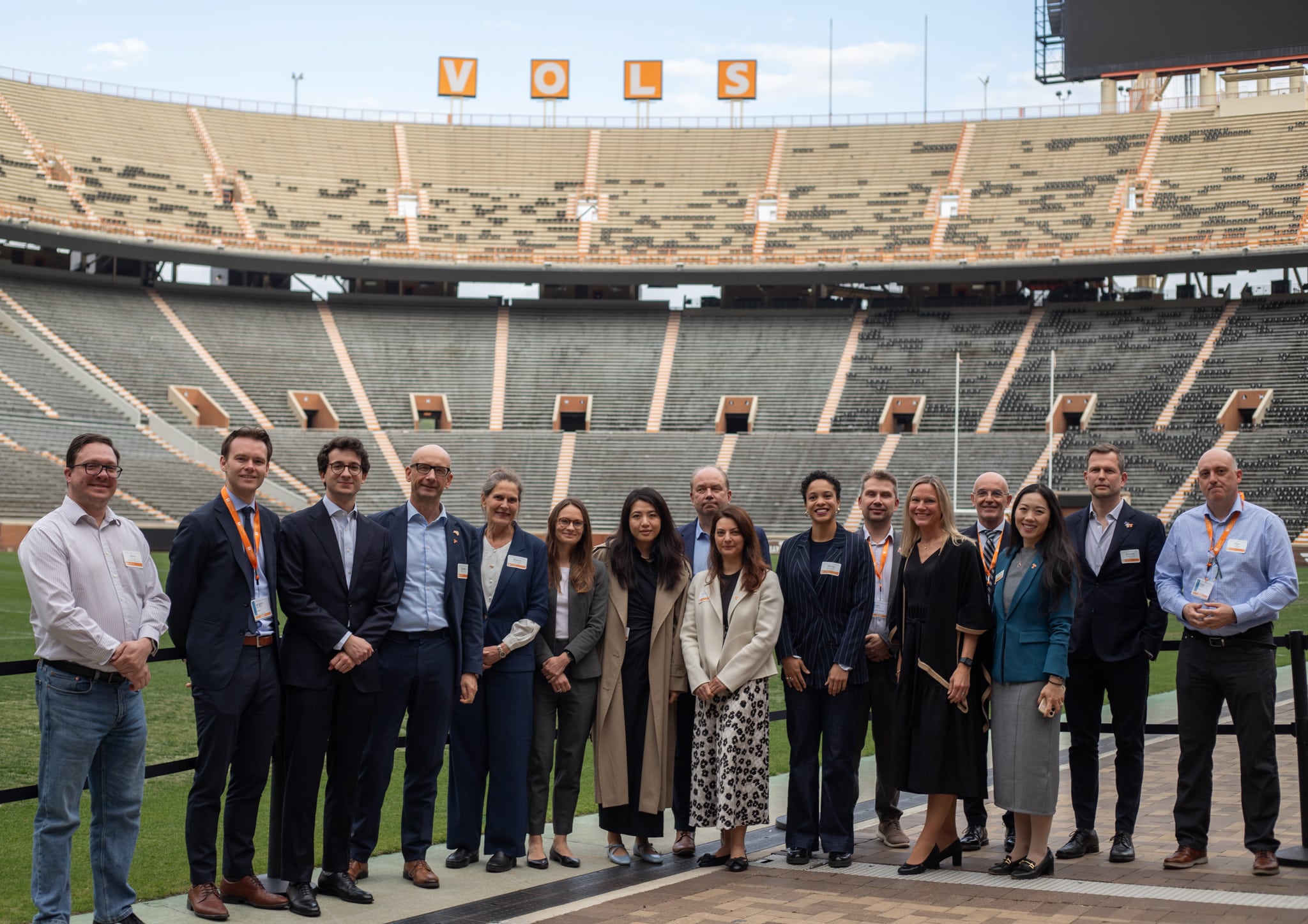 A group of people pose in front of an empty stadium. The word "VOLS" is spelled out at the top of the screen.