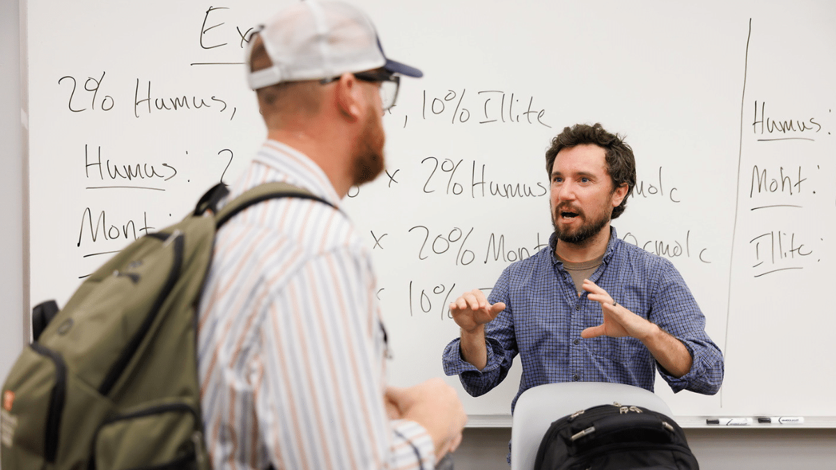 Faculty member talking to a student in front of a white board.