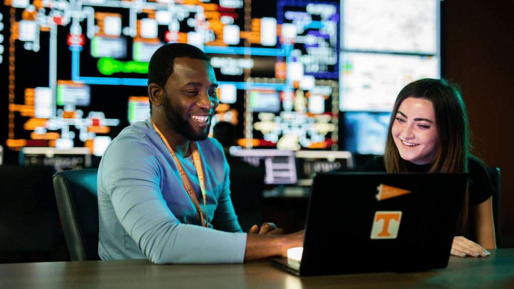 A man and a woman in a computer lab looking at a laptop.
